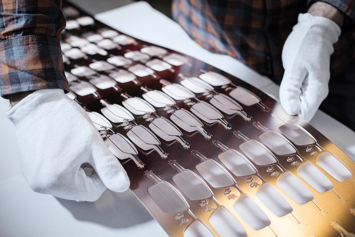 White-gloved hands lifting a sheet of cut OVVO metal frame fronts