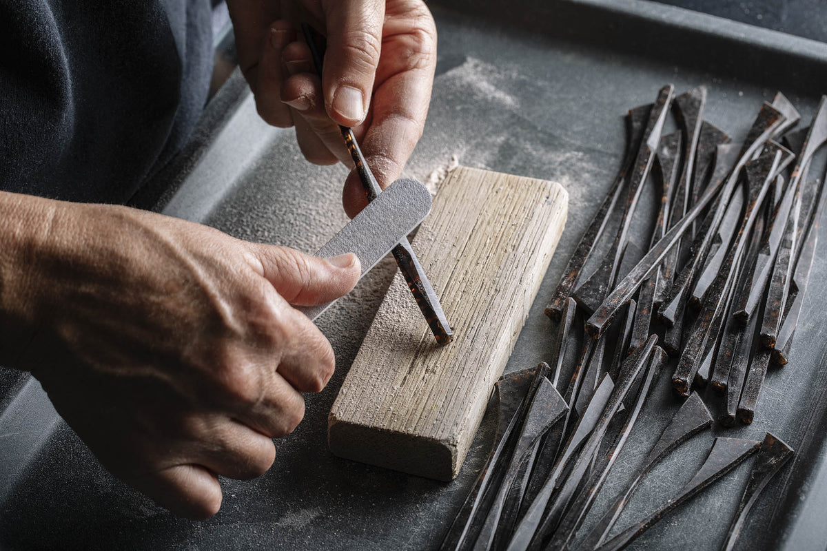 Craftsman's hands hand-filing a tortoise acetate temple over sanding block