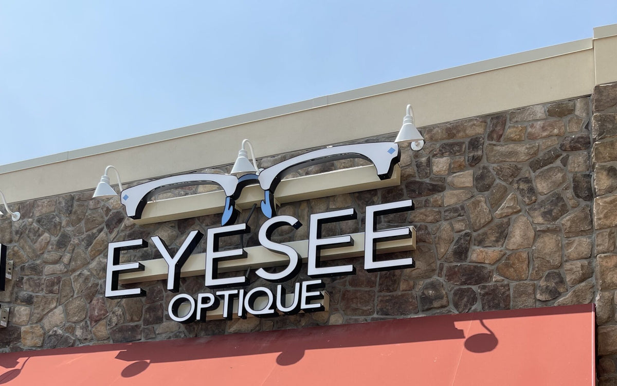 The Eye See Optique sign on the stone facade of the Dumfries shop, lit by daylight against a clear sky.